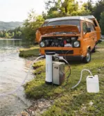 Aqua Peak 190 transportabelt osmoseanlæg placeret ved siden af en VW folkevognsbus, hvor de medfølgende 12V klemmetænger er monteret direkte på bilens batteri.